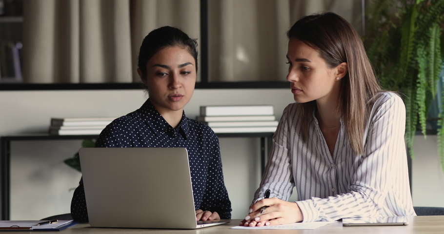 Focused millennial indian leader helping new worker with computer corporate software application in office. Motivated young mixed race employees developing project growth strategy, brainstorming ideas Royalty-Free Stock Footage #1071788746