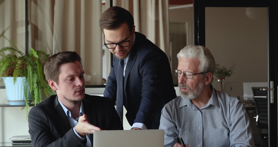 Concentrated male ceo executive manager reviewing sales or electronic report on computer with skilled young and old colleagues, discussing project problem solution or developing strategy together. Royalty-Free Stock Footage #1071788773