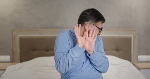 Disgusted mature man covering face on bed