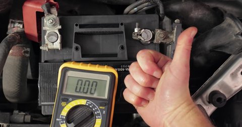 Car starter battery. Check battery voltage with electric multimeter. Good, electrician thumbs up, battery charged fully
