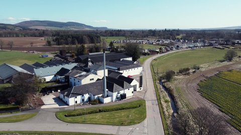 Aerial view of Fettercairn whisky distillery on a sunny spring day, Aberdeenshire, Scotland. Flying away from the distillery with Fettercairn town in the background.