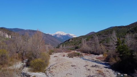 Drone shot going down to the river bridge and the snowy mountains in the background with a blue sky. In the spanish pyrenees.
