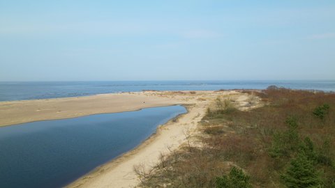 Aerial side shot of Vistula River ended in sand bank of Mewia Lacha Nature Reserve during sunny day and blue Baltic Sea in background.