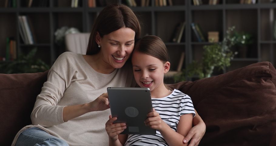 Loving mom and little daughter sit together on sofa at home with tablet device choose buy goods on internet, using education application for easy and funny learning, modern tech and generation concept Royalty-Free Stock Footage #1071802528