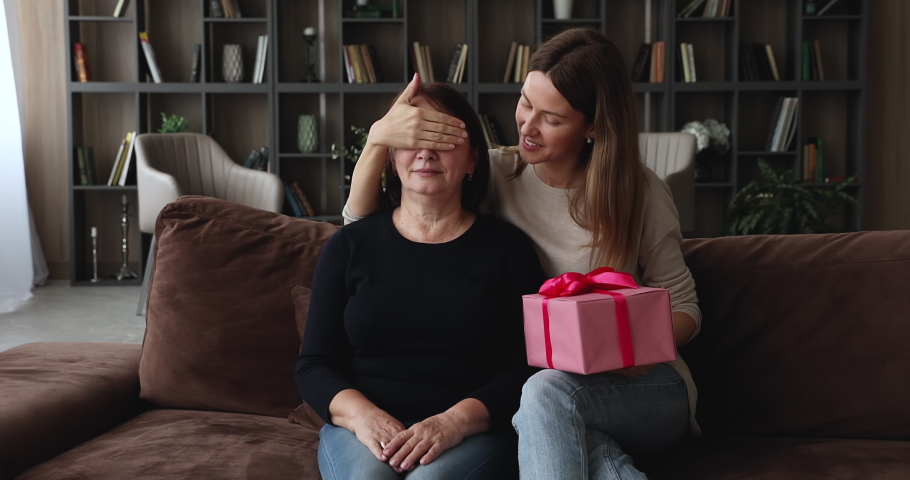 Caring grown up daughter congratulates birthday elderly mom, family sit on sofa in living room young woman make surprise give gift box to aged mom. Mothers Day congrats, life event celebration concept Royalty-Free Stock Footage #1071802687