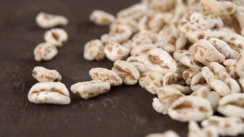 Puffed spelt wheat on a dark wooden background. Falling in slow motion. Raw cereal. Macro. Dolly shot