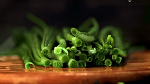 Super slow motion pieces of green onion cut off with a large knife. On a wooden background.Filmed at 1000 fps. 