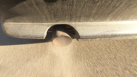 Emission from traffic. Exhaust pipe from a driving car in winter on a sunny day.