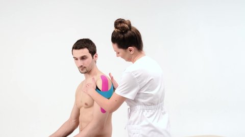 Shoulder treatment with kinesio tape. Physiotherapist applying elastic therapeutic tape to patient shoulder injury