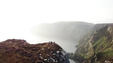 Aerial view of 3 people sitting on the edge of horn head cliff, County Donegal, Ireland