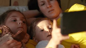 happy family at home. mom baby son and daughter watching online video on a smartphone gadget lying in bed at fun home. sunlight from window morning. happy family video chat online mom and baby kids