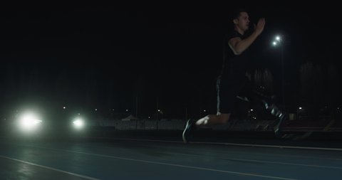 Cinematic shot of young disable man with legs prosthesis running with effort with racing auto behind on car track at night. Concept of handicapped people active lifestyle, determination, motivation.