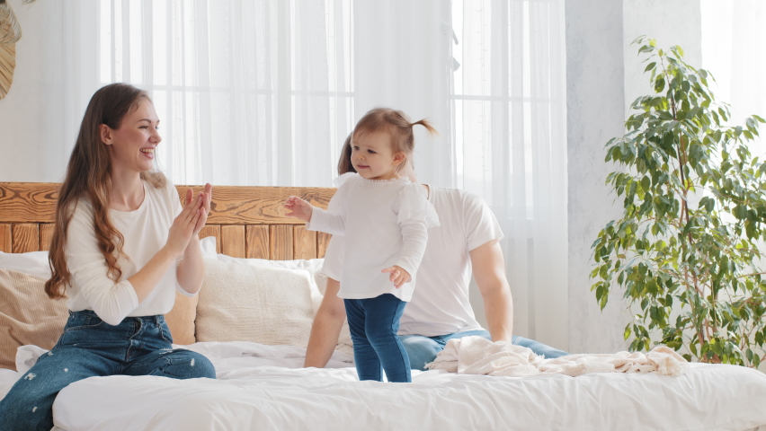 Family having fun at home bedroom in morning, little girl toddler dancing to music on bed father and mother support rejoice enjoying daughter dance child points with finger to camera mom waving hello Royalty-Free Stock Footage #1071824800