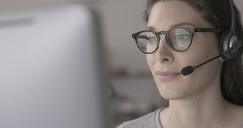 Woman connecting with her computer and video calling customers online, she is wearing a headset and nodding