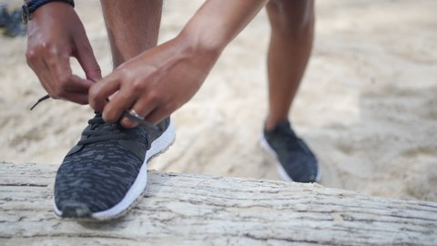 Close up of Athlete sportsman runner feet tying sport running shoes on the beach while jogging workout in sunny day. Healthy male runner do outdoor sport training exercise marathon running in summer.