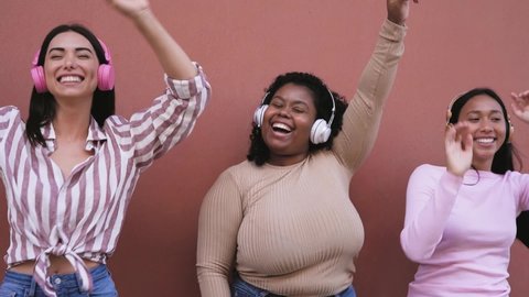 Happy young women having fun dancing and listening music with wireless headphones