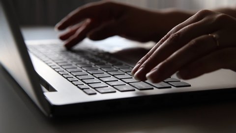 Female hands of a business woman using text input on the keyboard of a silver gray laptop, sitting at a home or office table. Working online concept, close-up 