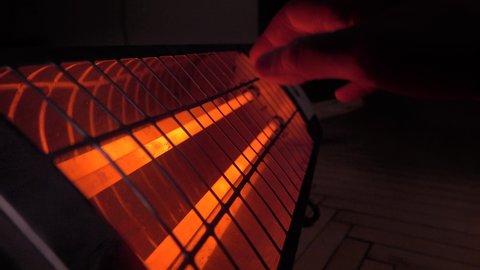 A man warms his hands over an infrared heater in a room in cold weather. Close-up