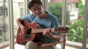 elderly Asian man resting playing guitar in the living room. - Powered by Shutterstock - Get 15% off with code: PIKWIZARD15