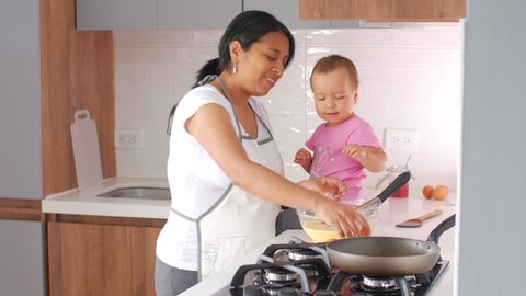 Hispanic pregnant mother and daughter cooking together at home in kitchen, happy together