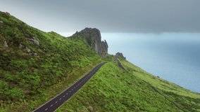 Overhead shot of asphalt road in green countryside of Flores Island, Azores, Portugal, Europe. Drone shot of green fields covering mountain hills at cloudy day, 4k footage