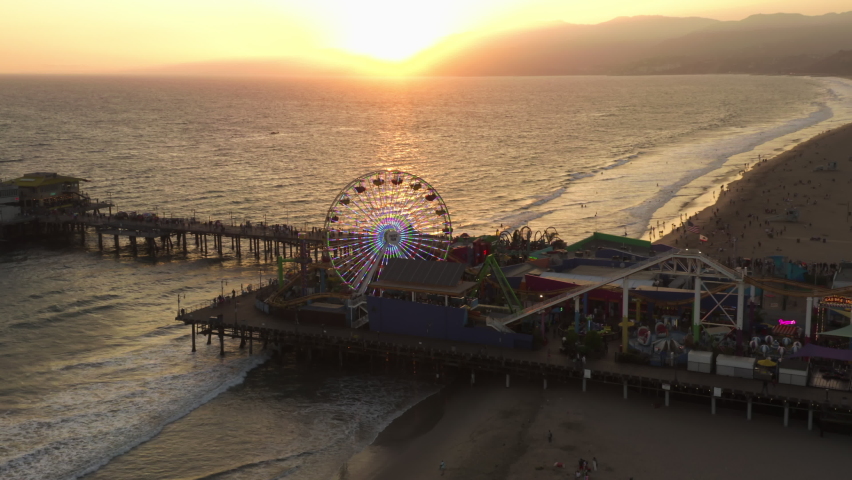 Pacific Park Theme Park on Santa Monica Pier with Ferrys Wheel in beautiful Golden Hour Sunset light over coastline, Aerial Wide Angle Shot, Lowering crane down Royalty-Free Stock Footage #1071872023