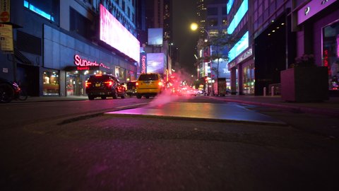 Low shot of cars driving at night with steam coming out of the ground in New York City Manhattan at Night 