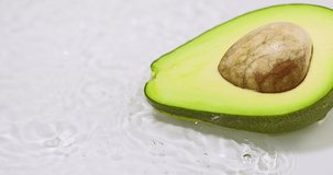 Ripe green avocado half, lying in flowing water. Natural organic fruit on white background. Vitamins, healthy eating