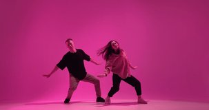 Dancing young couple show contemporary expressive dance, hip hop dancers performance in pink neon studio light