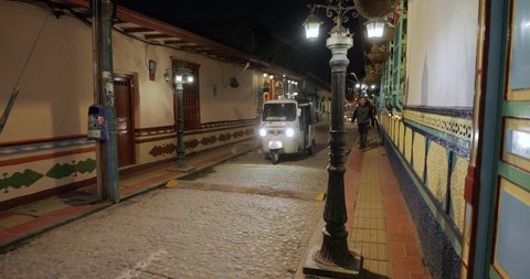 GUATAPE, COLOMBIA - CIRCA 2019: City view at night at the in a narrow street, tuktuk passing by in the popular touristic resort town Guatape, near Medellin, Antioquia
