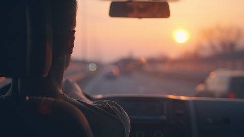 The young man driving the car along the highway on the sunset background