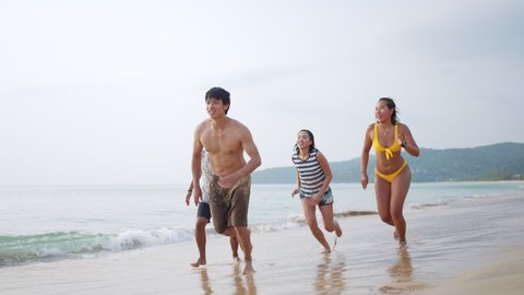 4K Group of Happy Asian man and woman friends running and playing together on tropical beach in sunny day. Male and female friendship enjoy and having fun outdoor lifestyle activity on summer vacation