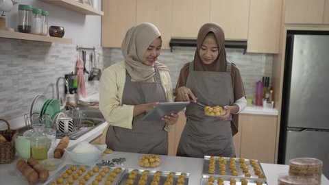 muslim small business owner making homemade nastar snack to sell. beautiful asian woman with partner cooking and holding tablet pc