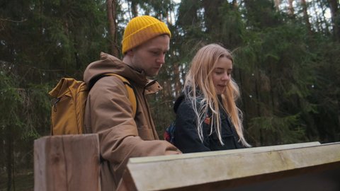 A young couple of travellers exploring the map of the forest. Finding the route