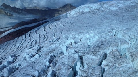 Aerail sideways cinematic icy frozen permafrost glacier on slopes of alpine mountains. Deep cracks, sharp ice tops. Clouds. Glacial period. Climate change, global warming ecology abstract footage 4k