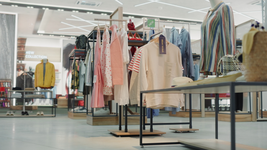Shopping Clothing Store Interior. Modern Fashionable Shop, Clothes for Every Taste. Stylish Brand Design, Fashionable Colors, Quality Sustainable Materials. No People. Low Dolly Establishing Shot Royalty-Free Stock Footage #1071893866