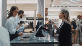 Clothing Store Checkout Cashier Counter: Beautiful Young Woman Buys Clothes from Friendly Retail Sales assistant, Paying with Contactless Credit Card. Fashion Shop with of Designer Brands. Medium Shot - Powered by Shutterstock - Get 15% off with code: PIKWIZARD15