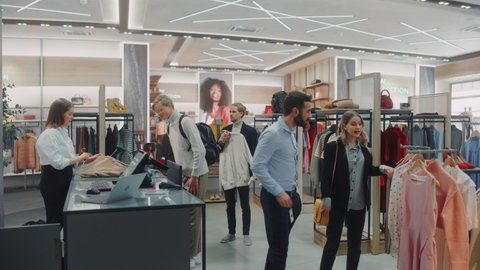 Clothing Store: Diverse Group of Costumers Shopping, buying Clothes and Merchandise at Checkout Cashier Counter. Retail Shopping Mall Assistant Helps Clients, Selling Brands. Wide Establishing Shot