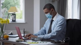 Young focused African American man in coronavirus face mask coughing messaging online and using label maker. Side view of concentrated professional manager with symptoms of Covid-19 in home office - Powered by Shutterstock - Get 15% off with code: PIKWIZARD15