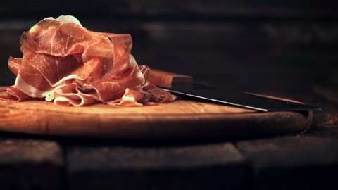 Super slow motion sliced into thin pieces of ham falls on a cutting board with a knife.Filmed at 1000 fps. On a wooden background. 