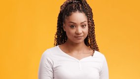 Studio portrait of young pretty african american lady with afro hairstyle feeling shy and embarrassed, orange background, slow motion