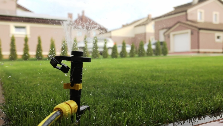 Lawn irrigation system, lawn sprinkler for watering grass in operation, sprays water in a circle to the left and right.  Royalty-Free Stock Footage #1071909355