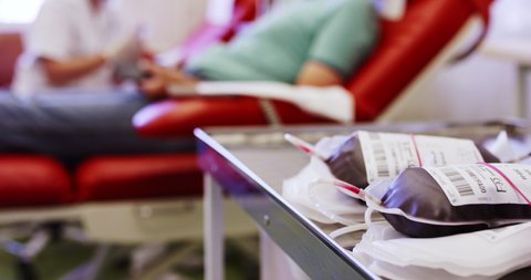Blood transfusion bags on table during donating, blurry donors in background