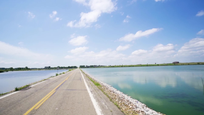 driving down 2 lane road passing lake on both sides