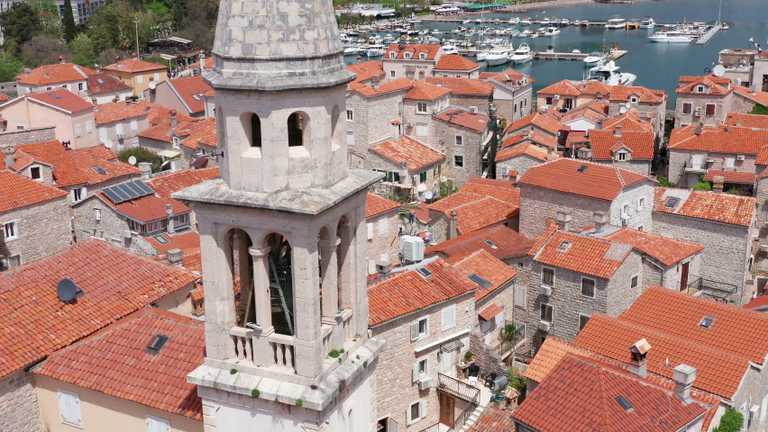 Old medieval town stone houses (Mediterranean architecture) - red roofs and church bell tower. Budva is the center of tourism in Montenegro and summer vacation destination. Aerial drone cityscape. Royalty-Free Stock Footage #1071916300