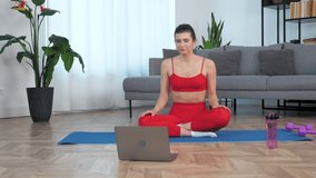 Smiling fit woman in sportswear sits on yoga mat greets waving hand listen fitness trainer, study online remote video conference call webcam chat laptop computer, watch distance sport education lesson