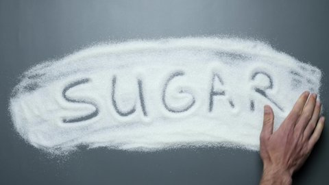Hand writing word sugar on background of white sugar. Sugar kills. Unhealthy eating. Prevent cancer and diabetes mellitus disease. No sugar. Stop diabetes