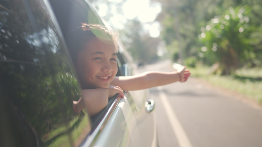 Happy Asian family enjoy and having fun together with outdoor lifestyle activity on road trip vacation. Little child girl kid sit in the car with pull her face and hand out of car window in summer day Royalty-Free Stock Footage #1071926026