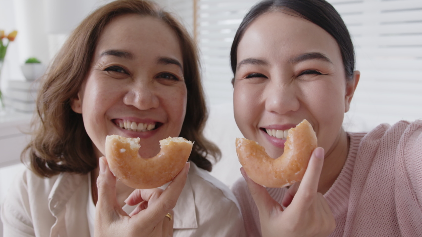 Portrait attractive beautiful two people family use cellphone take photo picture doughnut video story smiley overjoy donut at sofa couch living room have good time together quarantine social distance.