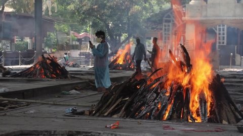 New Delhi, India, April 27, 2021 Family member pays their last rites to those who died from the COVID-19 coronavirus disease as other funeral pyres seen during the mass cremation 